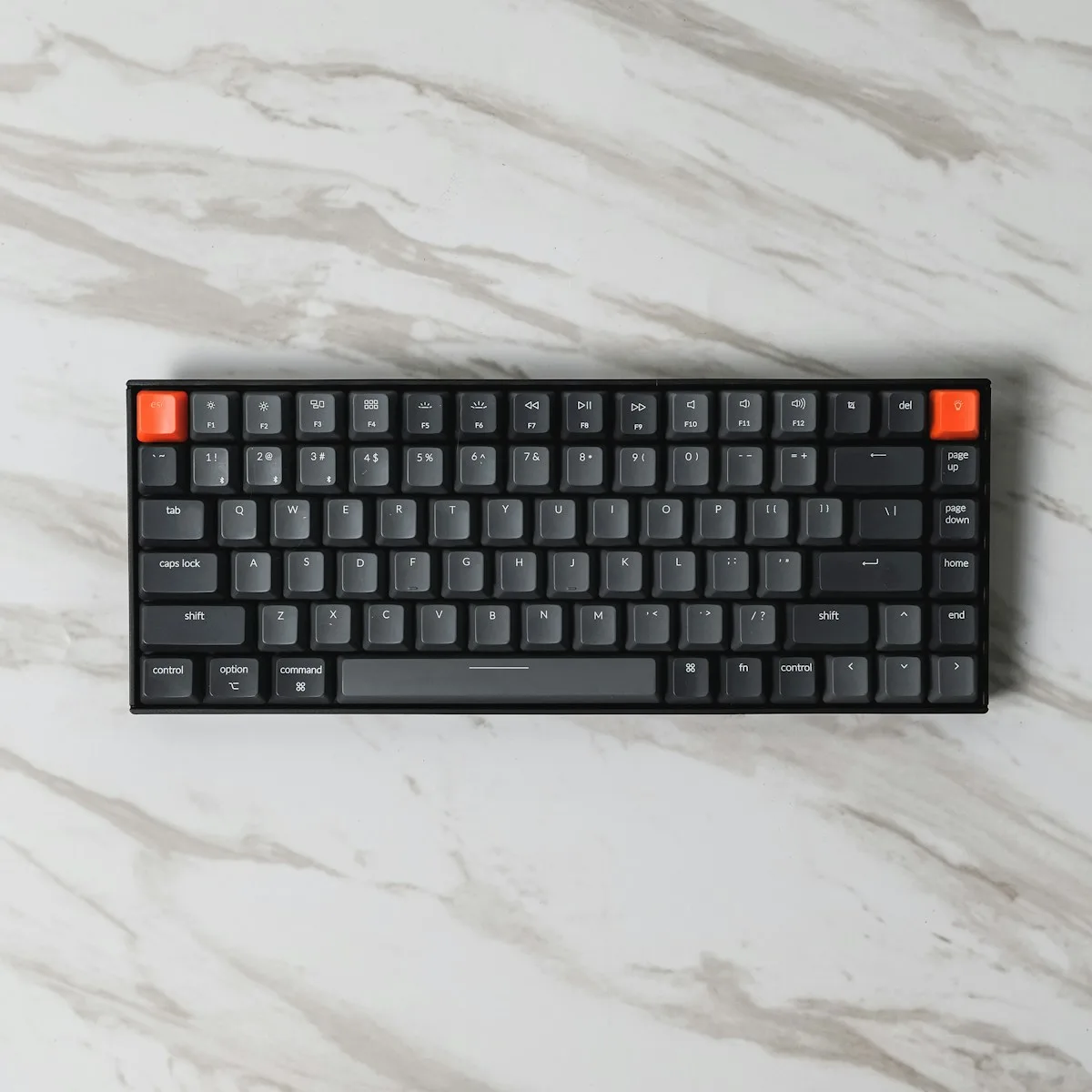 Compact black mechanical keyboard with orange accent keys on a marble desk
